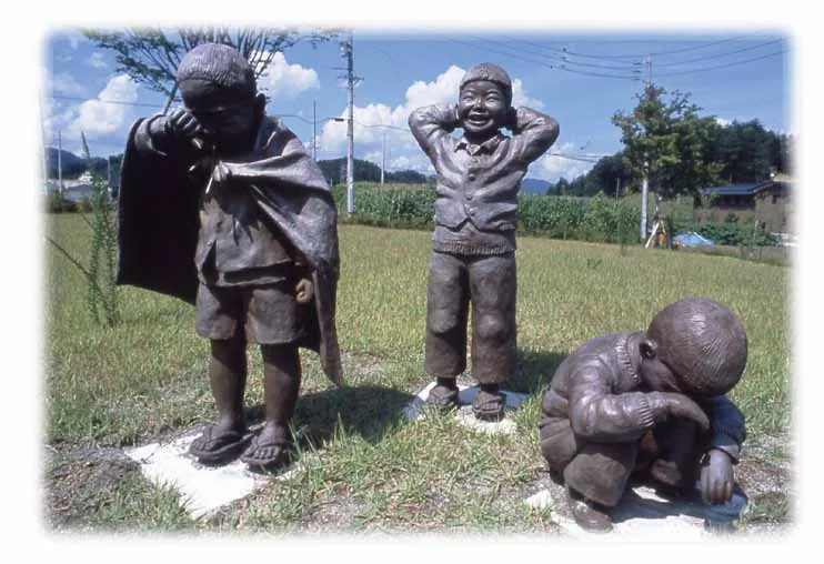 Bronze sculpture of three boys on a lawn: one covering his face, one laughing with his hands behind his head, and one crouching