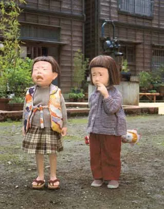 The original dolls: a crying girl and a girl sucking her finger, standing side by side in front of a school building