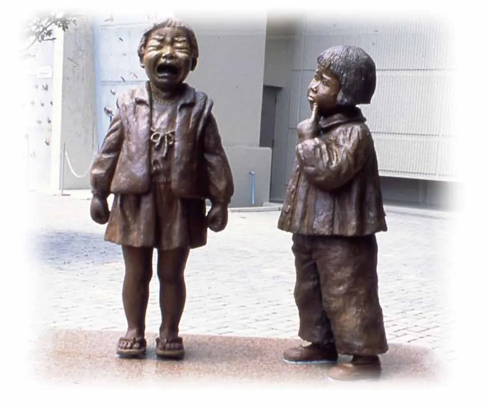Bronze sculpture of a girl in tears and a girl sucking her finger, standing on paving stones in front of a building
