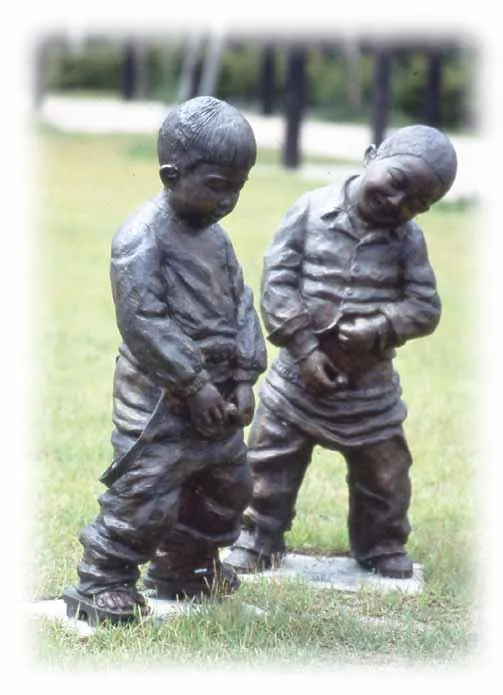 Bronze sculpture of two boys standing side by side on a lawn