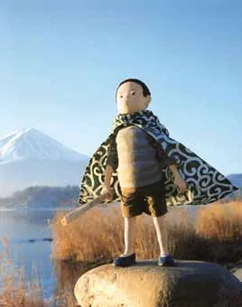 The original doll: a boy in an arabesque-patterned cape standing on a rock, with Mount Fuji and a lake behind him