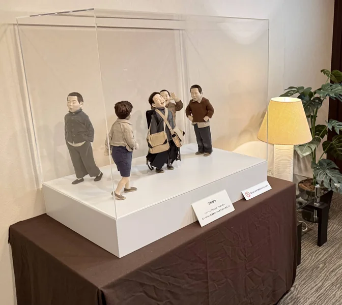 台の上のアクリルケースの中で、空を見上げて笑う作品「学校帰り」の人形と、横のスタンドの明かり