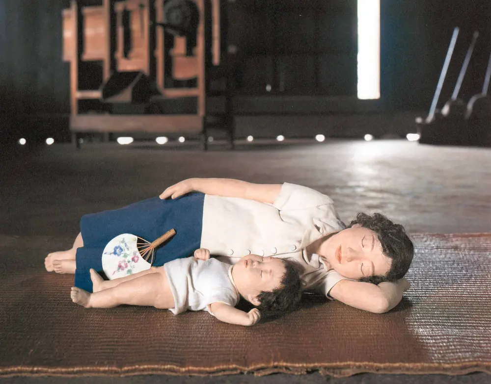 板の間に寝ころんで、昼寝をする母と子の人形