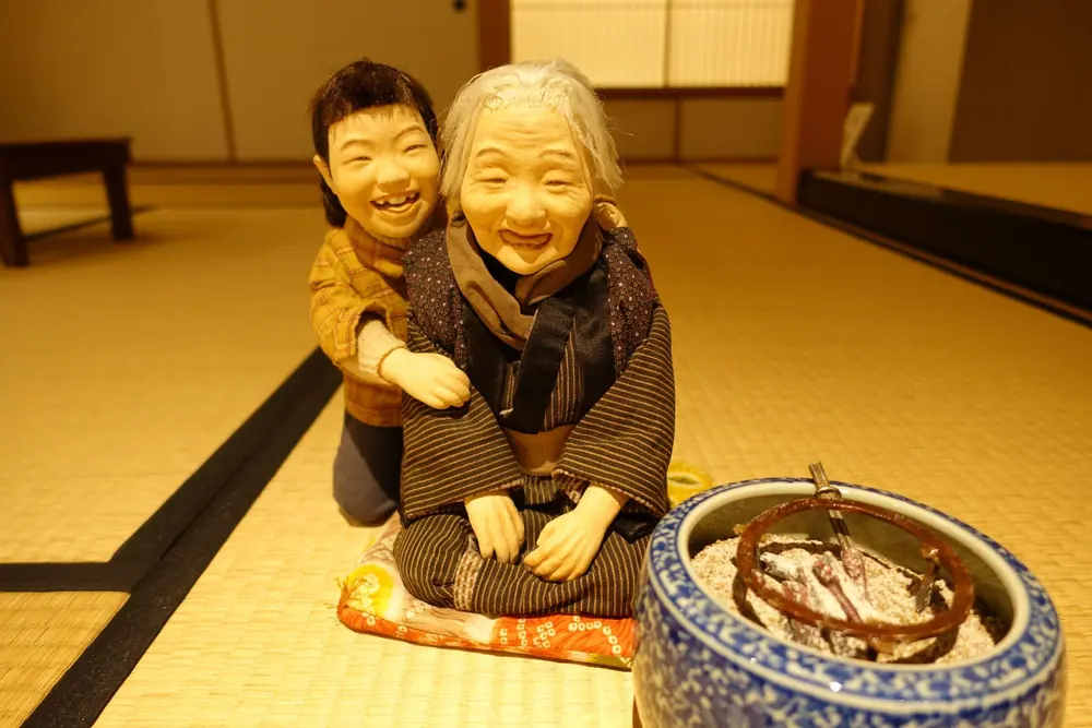 畳に座るおばあちゃんと、背中から抱きついて笑うこどもの人形