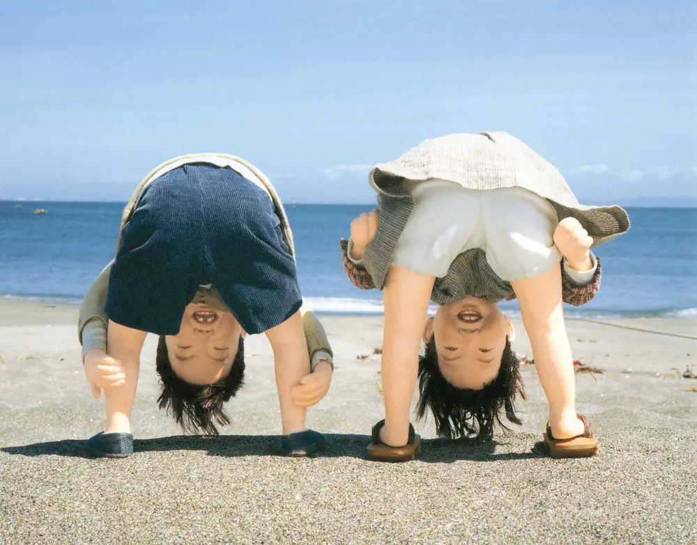 浜辺で、股の間からのぞくふたりのこどもの人形