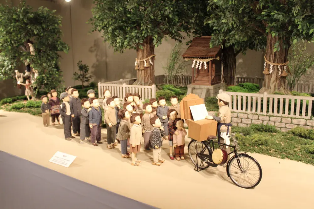 展示室の神社のジオラマで、自転車の紙芝居を囲むこどもたちの人形