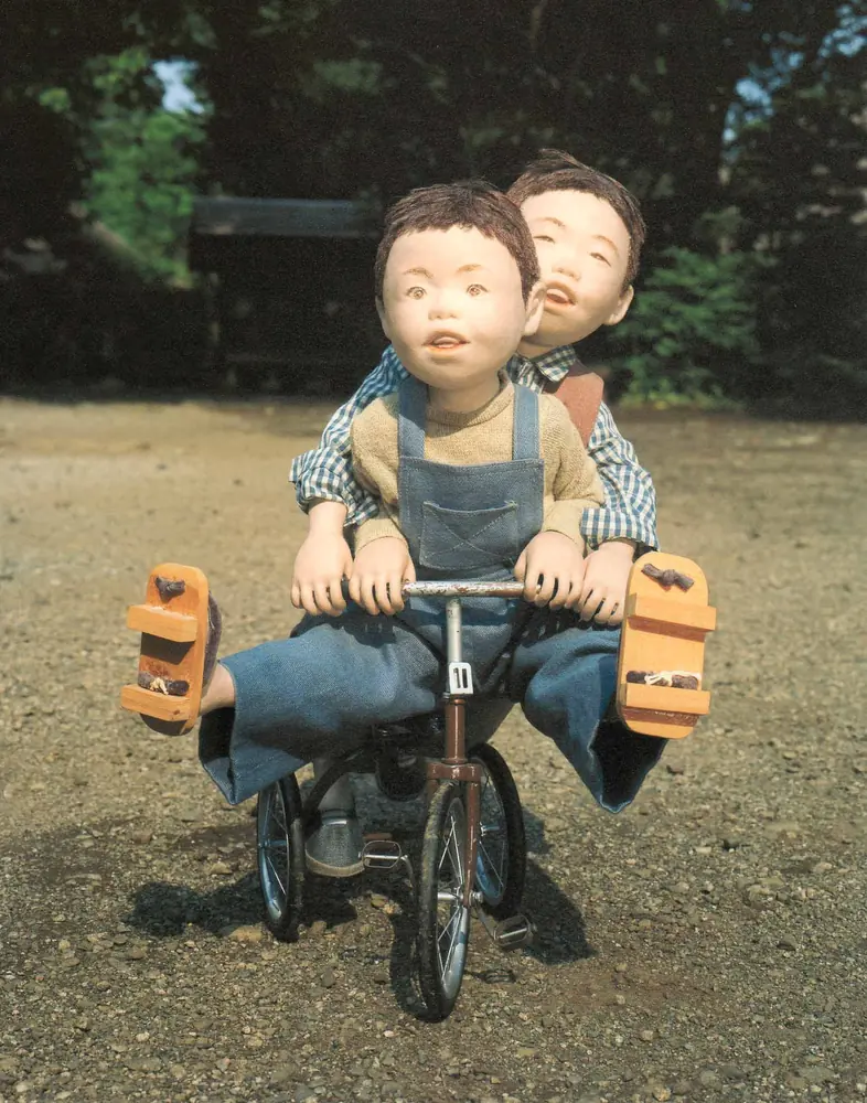 ひとつの三輪車に二人で乗る、男の子の人形