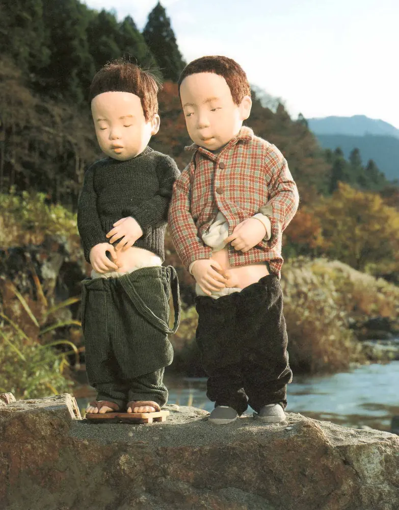 川べりの岩の上に並んで立つ、ふたりの男の子の人形