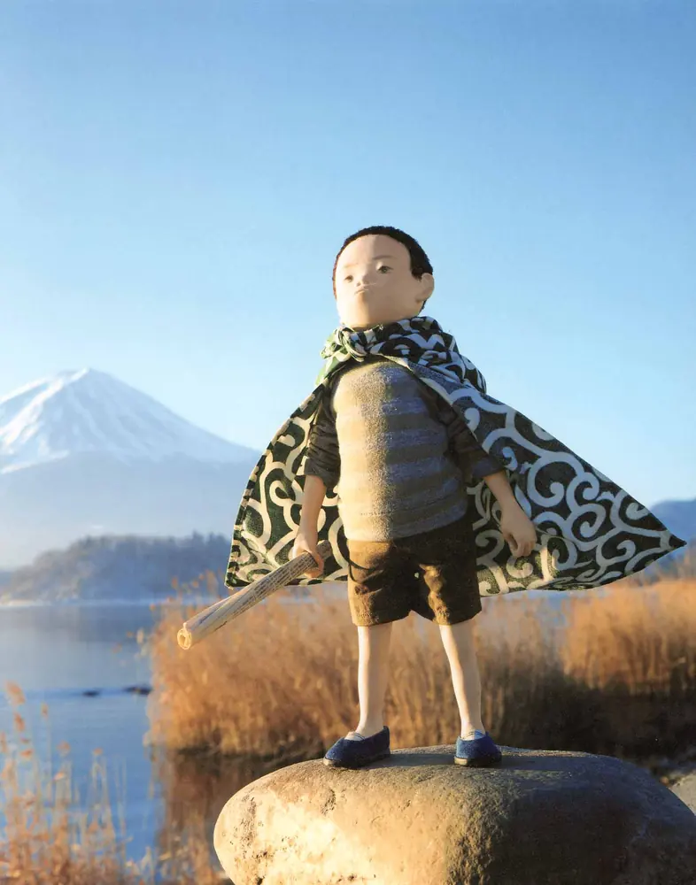 富士山と湖を背に、マントをはおって岩の上に立つ男の子の人形