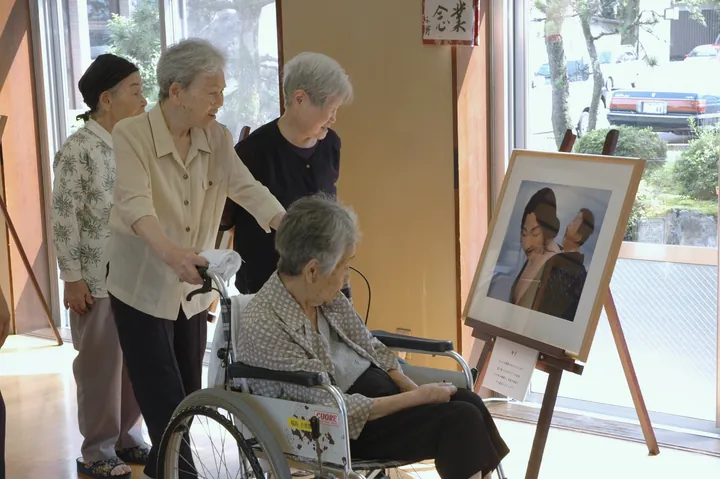 三脚に立てた写真パネルの前で、車いすの方と付き添いの方が展示を見ている様子