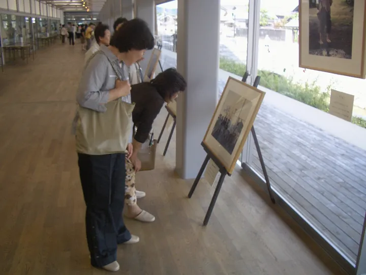 ガラス張りの通路で、三脚に立てた写真パネルをのぞきこむ人たち